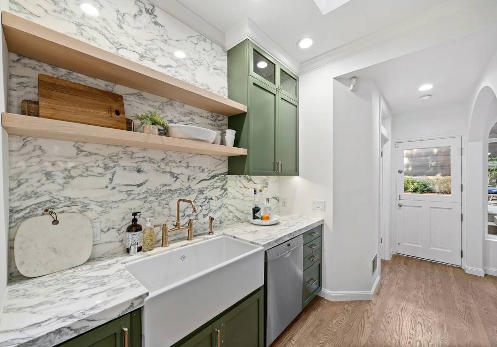 A kitchen with green cabinets and white marble counters.