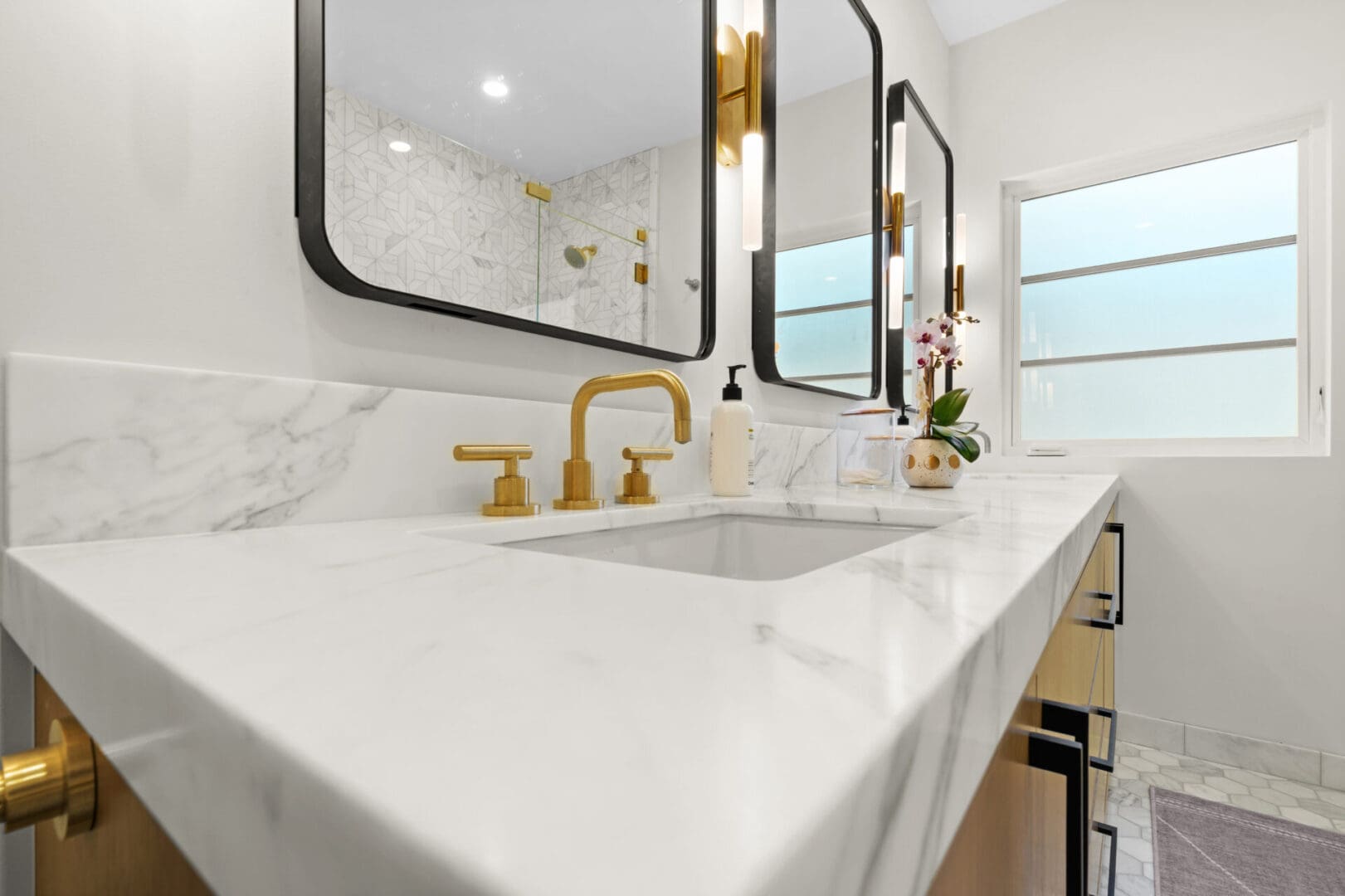 A bathroom with marble counter tops and gold fixtures.