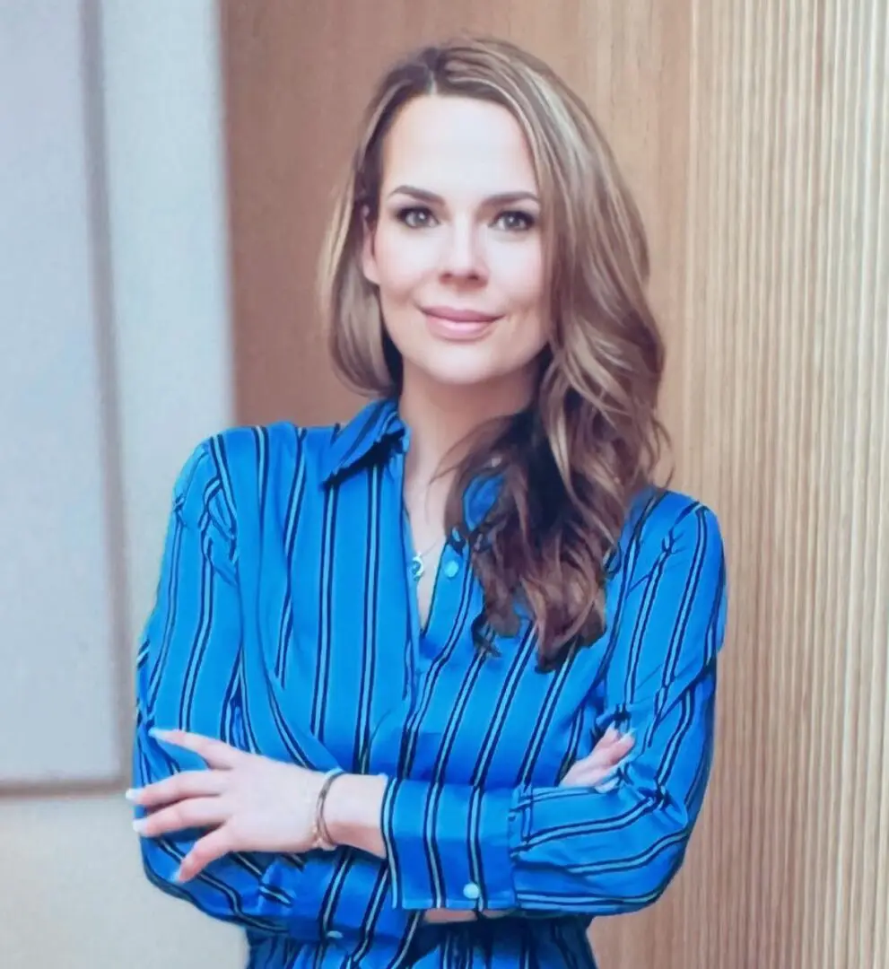 A woman in blue shirt standing with her arms crossed.